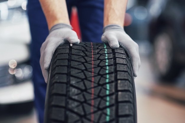 Closeup of mechanic hands pushing a black tire in the workshop