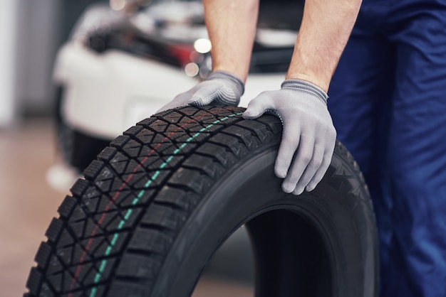 Free photo closeup of mechanic hands pushing a black tire in the workshop