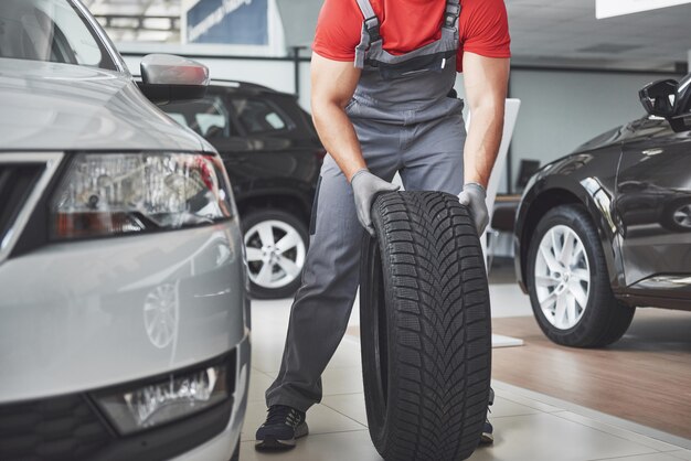 Closeup of mechanic hands pushing a black tire in the workshop.