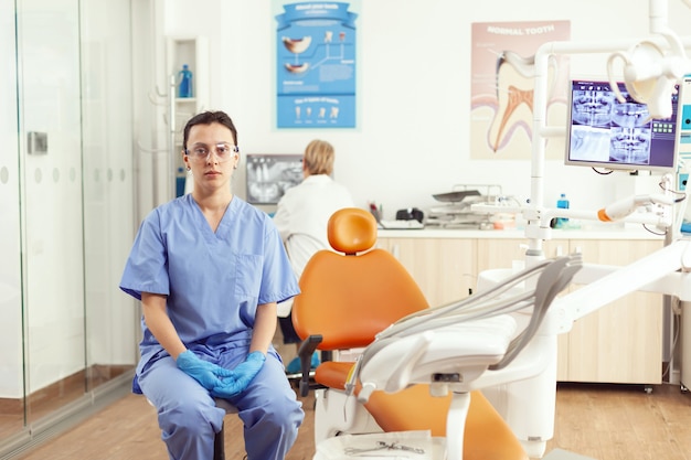 Крупным планом фельдшера, сидящего на стуле в офисе больницы, ожидая больного пациента, чтобы исследовать стоматологическую проблему во время стоматологического приема