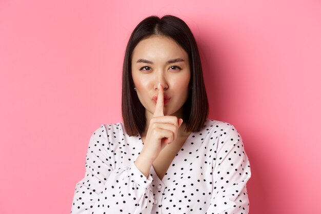 Closeup of mysterious asian woman hiding a secret hushing and telling to keep quiet standing over pi...