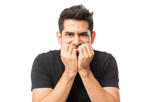 Closeup of nervous young man biting finger nails against white background