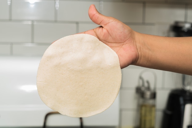 Крупным планом человека, держащего тонкое круглое тесто на кухне при свете