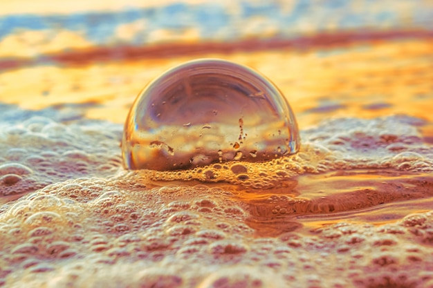 無料写真 夕方の日没時に海に囲まれた砂の上の透明なボールのクローズアップ