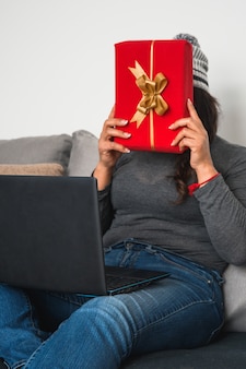 Крупным планом женщина разговаривает со своими друзьями на ноутбуке и показывает им красную подарочную коробку