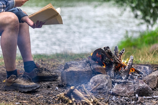 Бесплатное фото Крупный план костра с человеком, читающим книгу на заднем плане в природе