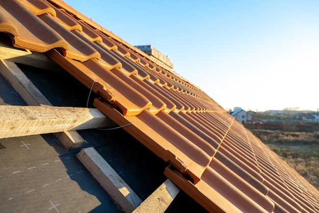 Крупным планом металлический монтажный анкер для установки желтой керамической черепицы, установленной на деревянных досках, покрывающих крышу строящегося жилого дома.