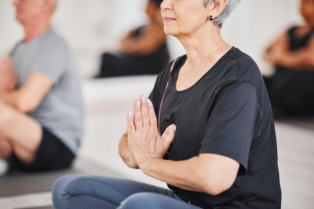 蓮華座​に​座って​、​クラス​で​の​トレーニング中​に​瞑想している​年配​の​女性​の​クローズアップ