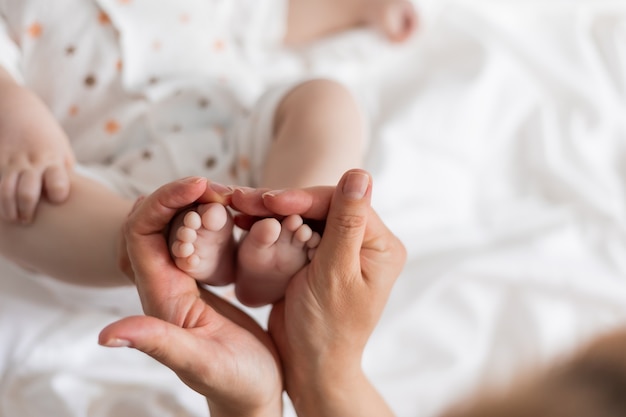 Крупным планом босые ноги новорожденного в руках матери на белом фоне вид сверху