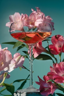 파란색에 분홍색과 마젠타색 알스트로메리아 꽃으로 둘러싸인 유리잔에 와인이나 칵테일을 닫습니다
