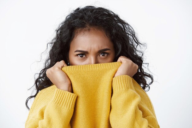 Closeup offended sulking african american pretty girlfriend with black curly hair frowning upset stare angry or jealous camera hiding face in yellow sweater unwilling talk acting childish