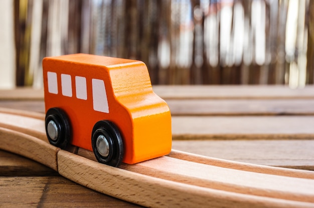 Closeup of an orange wooden toy car on the tracks under the lights