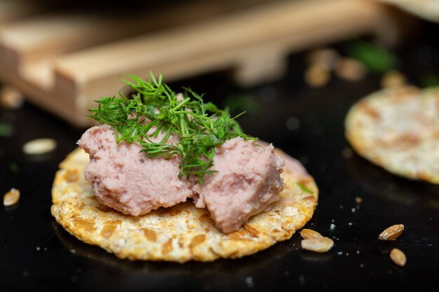 Closeup of pate on a cracker with herbs on the table under the lights with a blurry