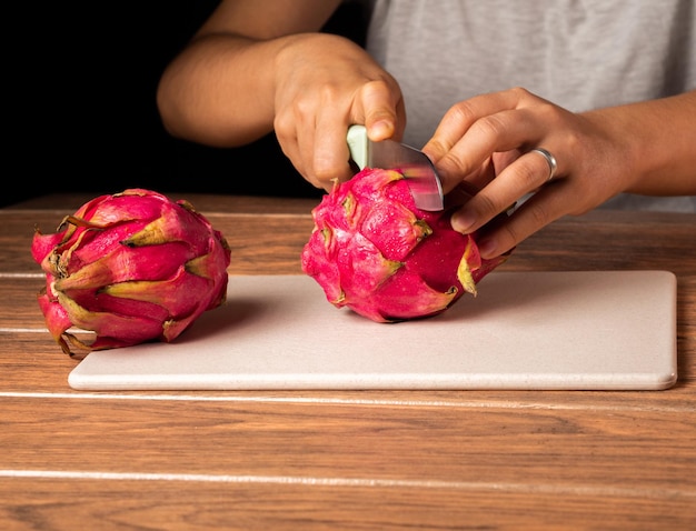 Closeup of a person cutting a red dragon fruit in half on a cutting board on the table