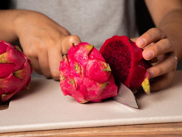 Closeup of a person cutting a red dragon fruit in half on a cutting board on the table
