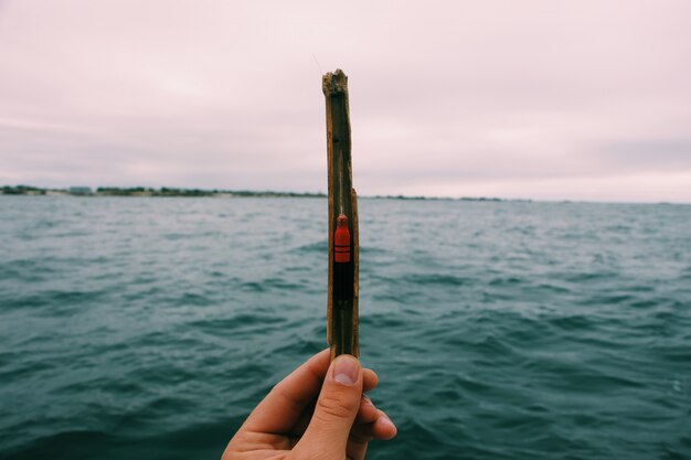 Closeup of a person holding a fishing bait with a blurred sea and a cloudy sky