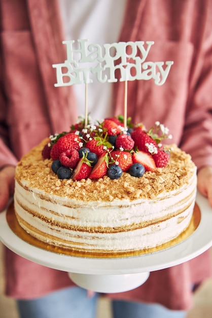 「お誕生日おめでとう」トッパーでフルーティーなケーキを持っている人のクローズアップ