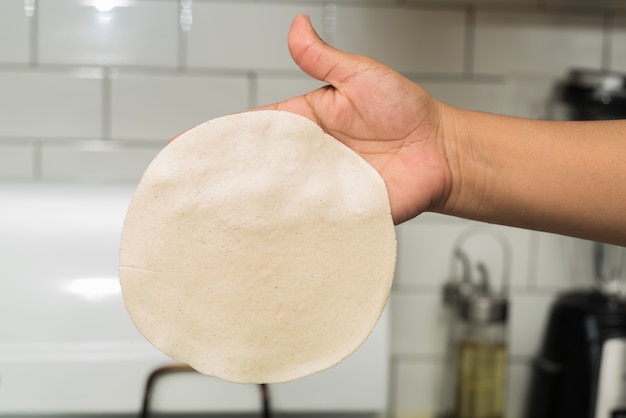 Closeup of a person holding a thin round dough in a kitchen under the lights