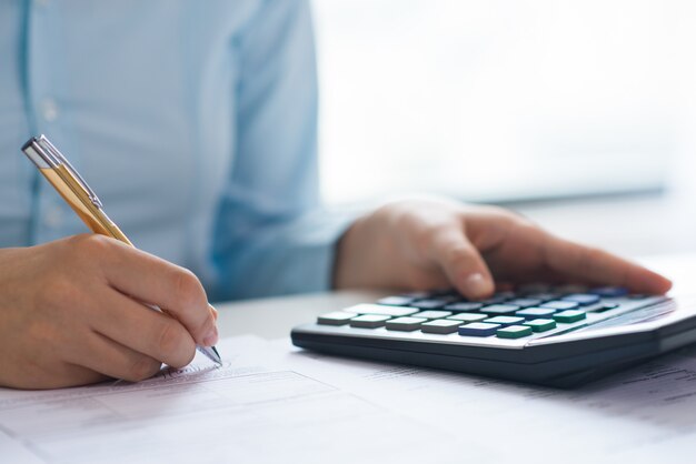 Closeup of person signing document and using calculator