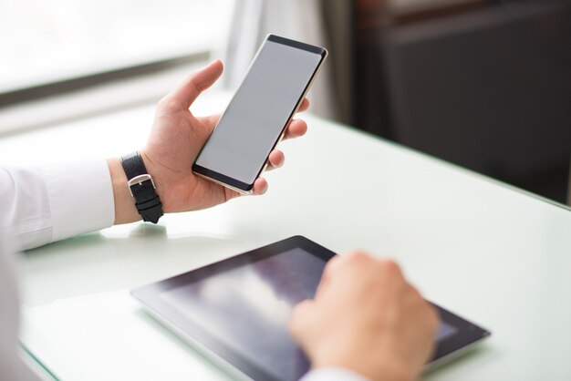 Closeup of person using smartphone and tablet computer at table