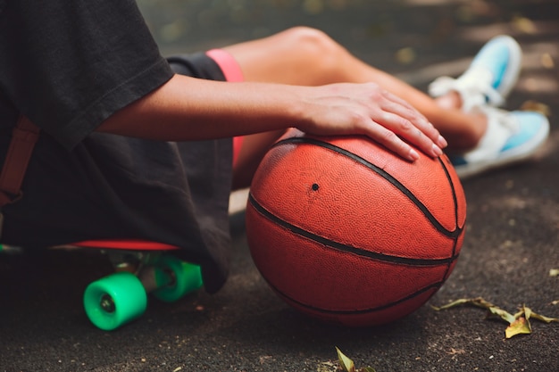 Closeup photo basketball ball with girl sitting on plastic orange penny shortboard on asphalt