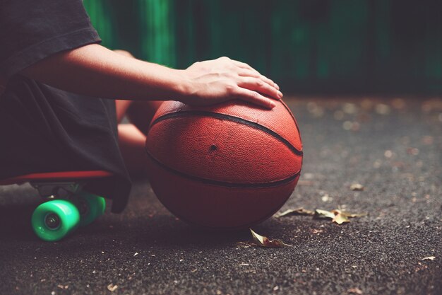 Closeup photo basketball ball with girl sitting on plastic orange penny shortboard on asphalt