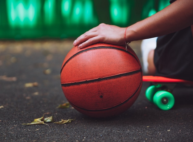 Крупным планом фото баскетбольный мяч с девушкой, сидящей на пластиковой оранжевой копеечке на асфальте