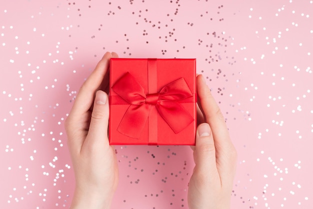 Closeup photo of female hands giving red giftbox over pastel color shimmer background