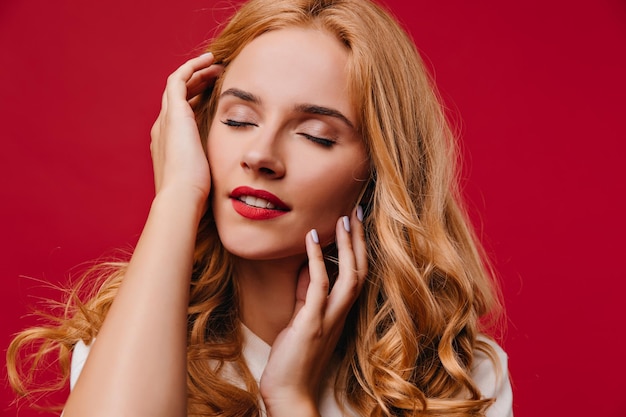 Closeup photo of pleasant girl with long wavy hair Studio shot of beautiful relaxed woman isolated on red background