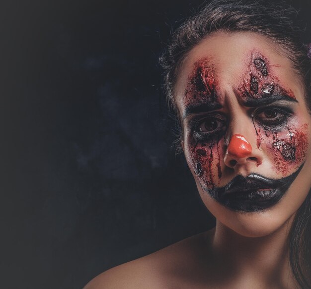 Фотосессия крупным планом жуткой девушки со злым клоунским макияжем в темной фотостудии.