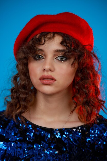 Closeup photo of young lady wearing red hat and looking at the camera on blue background High quality photo