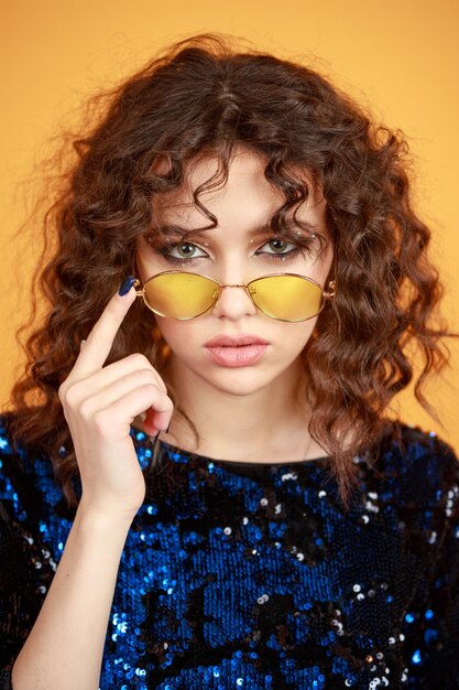 Closeup photo of young lady wearing sunglasses and looking at the camera on orange background High quality photo