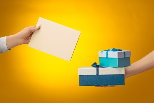 closeup picture of man and woman's hands with gift box on yellow background