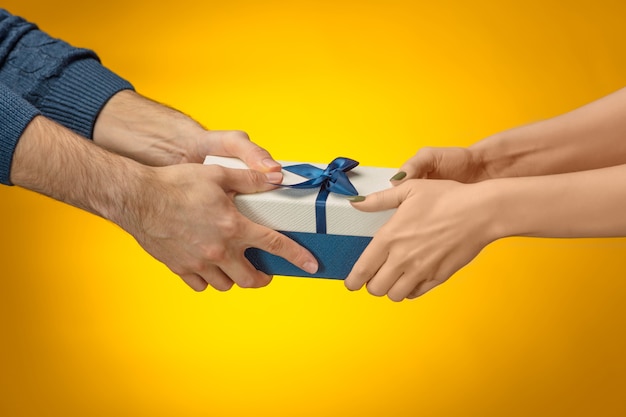 closeup picture of man and woman's hands with gift box on yellow background