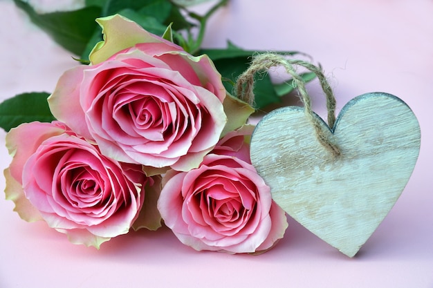 Closeup picture of pink roses with a heart-shaped wooden ornament