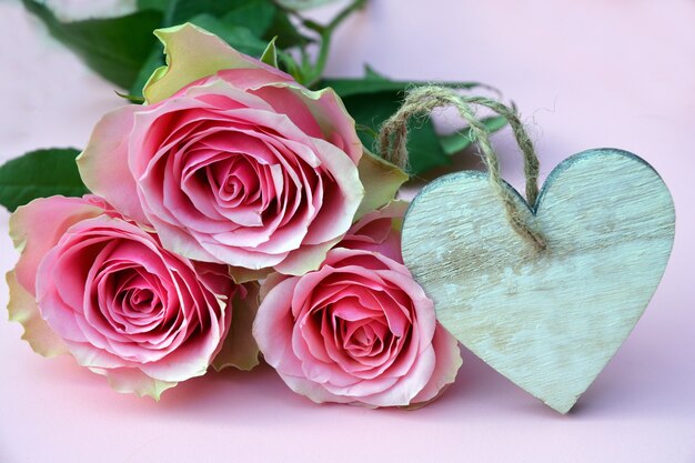 Closeup picture of pink roses with a heart-shaped wooden ornament