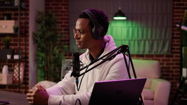 Closeup of podcast presenter reading questions from audience using laptop to woman content creator in online live broadcast from home studio. African american internet radio host recording interview.