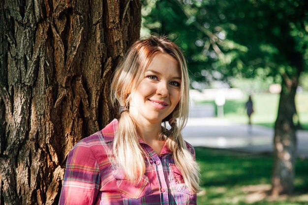 Closeup portrait adult shining blonde woman with sun on face and with pigtails looking into camera l...