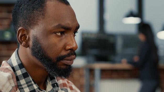 Closeup portrait of african american software developer working focused looking at computer screen while typing. System engineer writing ai code while colleagues are programming in background.