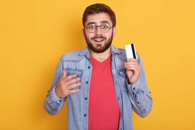 Closeup portrait of astonished bearded man with credit card in hands, looks excited, found out about huge amount of money on card