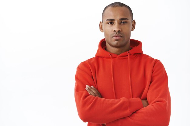 Closeup portrait of athletic seriouslooking handsome african american in red hoodie cross hands chest look camera determined couch saying team stay home during quarantine white background