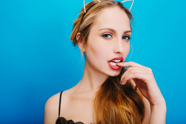 Closeup portrait of attractive girl with long blonde hair, cat ears in diamonds, sexy looking and biting her finger. Nice makeup.