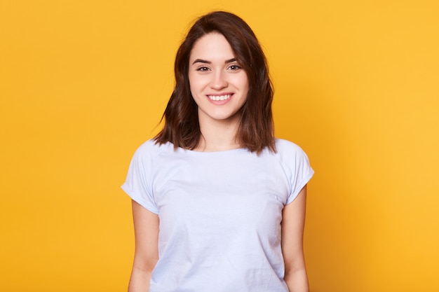 Closeup portrait of attractive woman stands smiling isolated over yellow