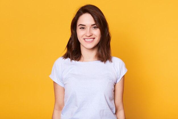 Closeup portrait of attractive woman stands smiling isolated over yellow