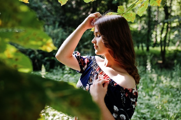 Closeup portrait of a beautiful brunette in dress next to the leaves