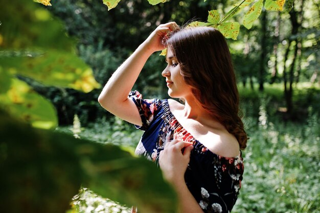 Closeup portrait of a beautiful brunette in dress next to the leaves