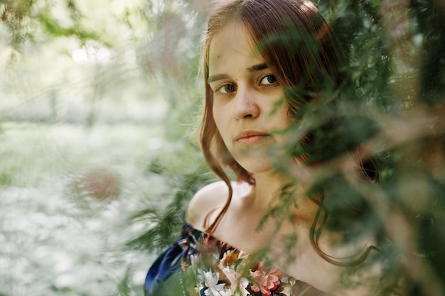 Closeup portrait of a beautiful brunette in dress next to the leaves
