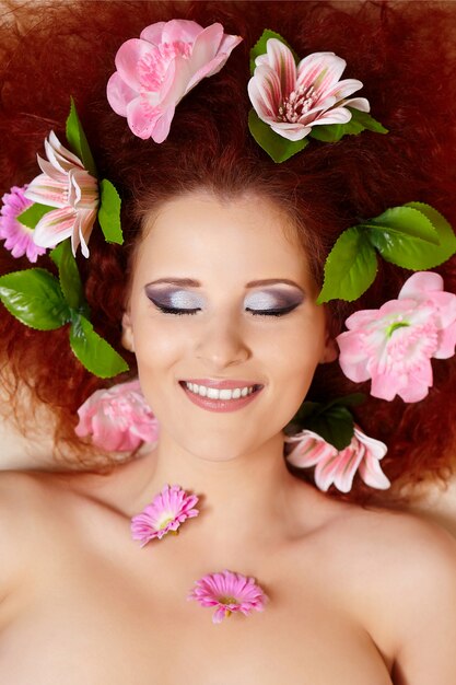 closeup portrait of beautiful smiling redhead ginger woman face with colorful flowers in hair