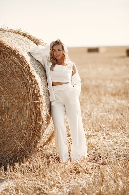 Closeup portrait of beautiful smiling woman. The blondee on a bale of hay. A wheat field on the background.