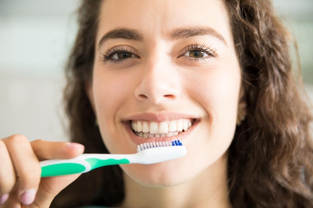 Крупным планом портрет красивой молодой женщины, чистящей зубы в стоматологической клинике